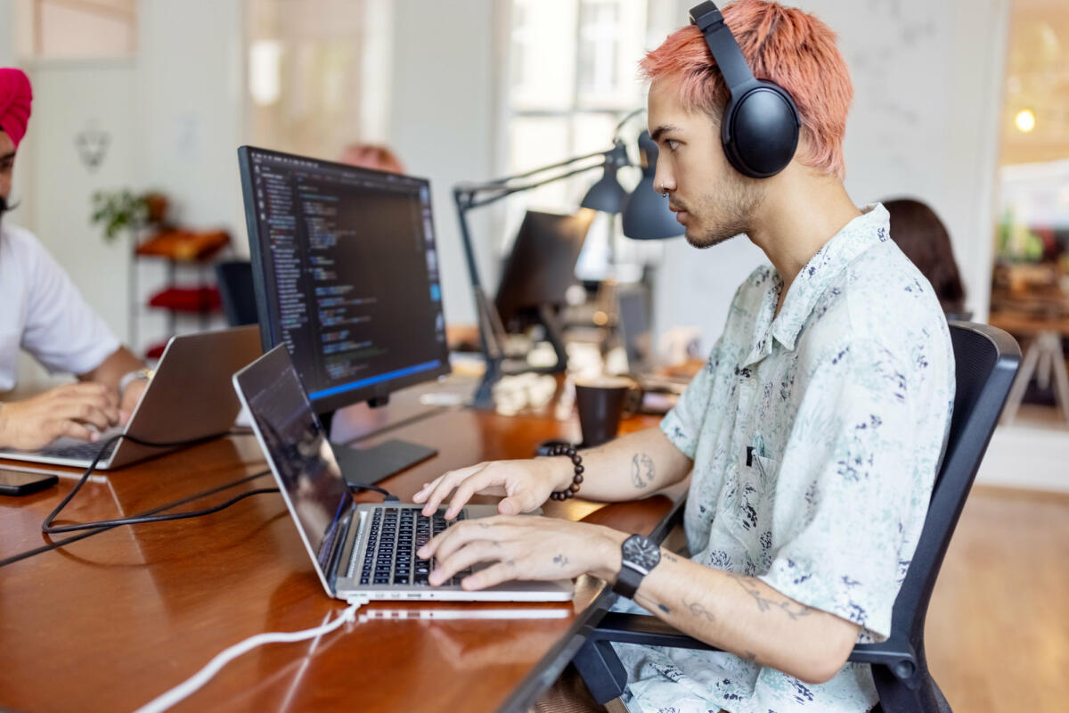 Junger Mann mit Kopfhörern bei der Arbeit am Computer in einem Startup-Büro © Luis Alvarez / Getty Images