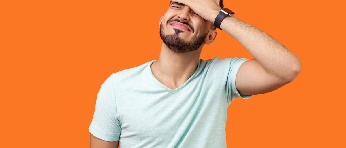 Porträt eines verzweifelten brünetten Mannes mit Bart in weißem T-Shirt, der das Gesicht mit der Hand bedeckt. © Khosrork / Getty Images