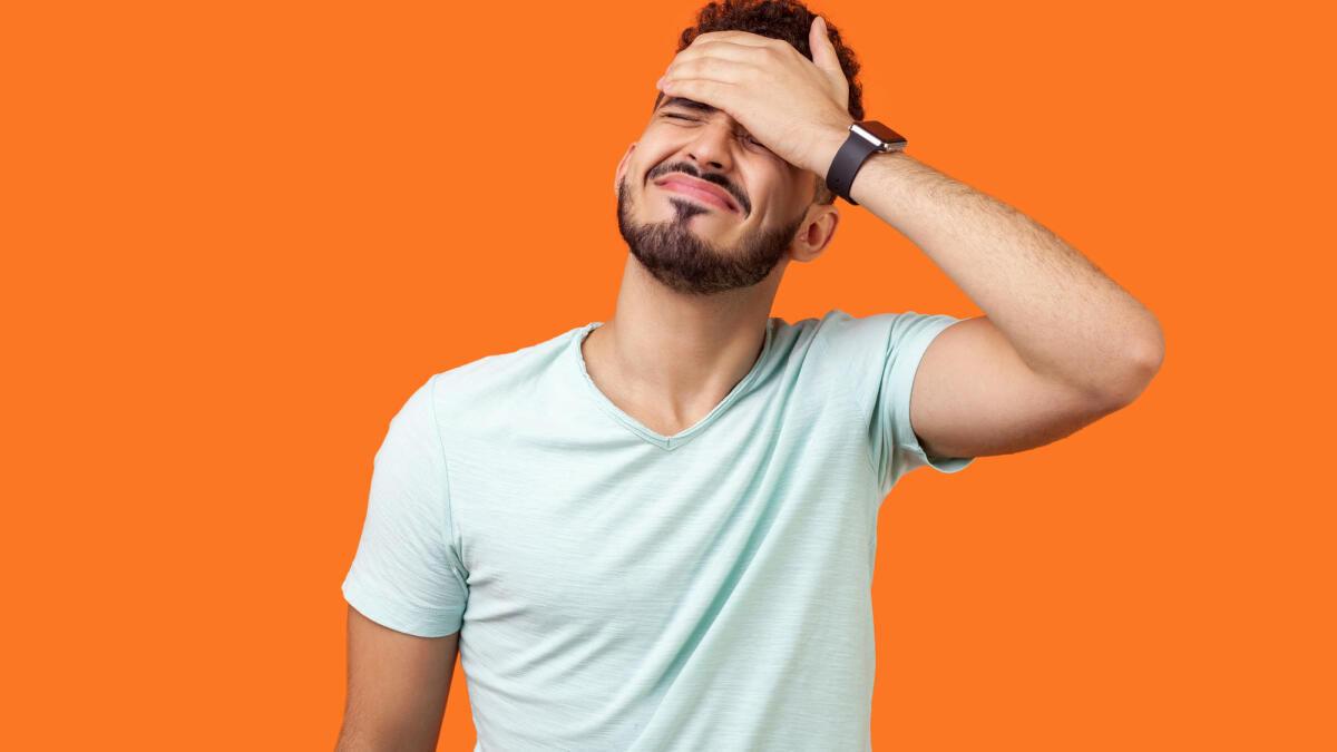 Porträt eines verzweifelten brünetten Mannes mit Bart in weißem T-Shirt, der das Gesicht mit der Hand bedeckt. © Khosrork / Getty Images