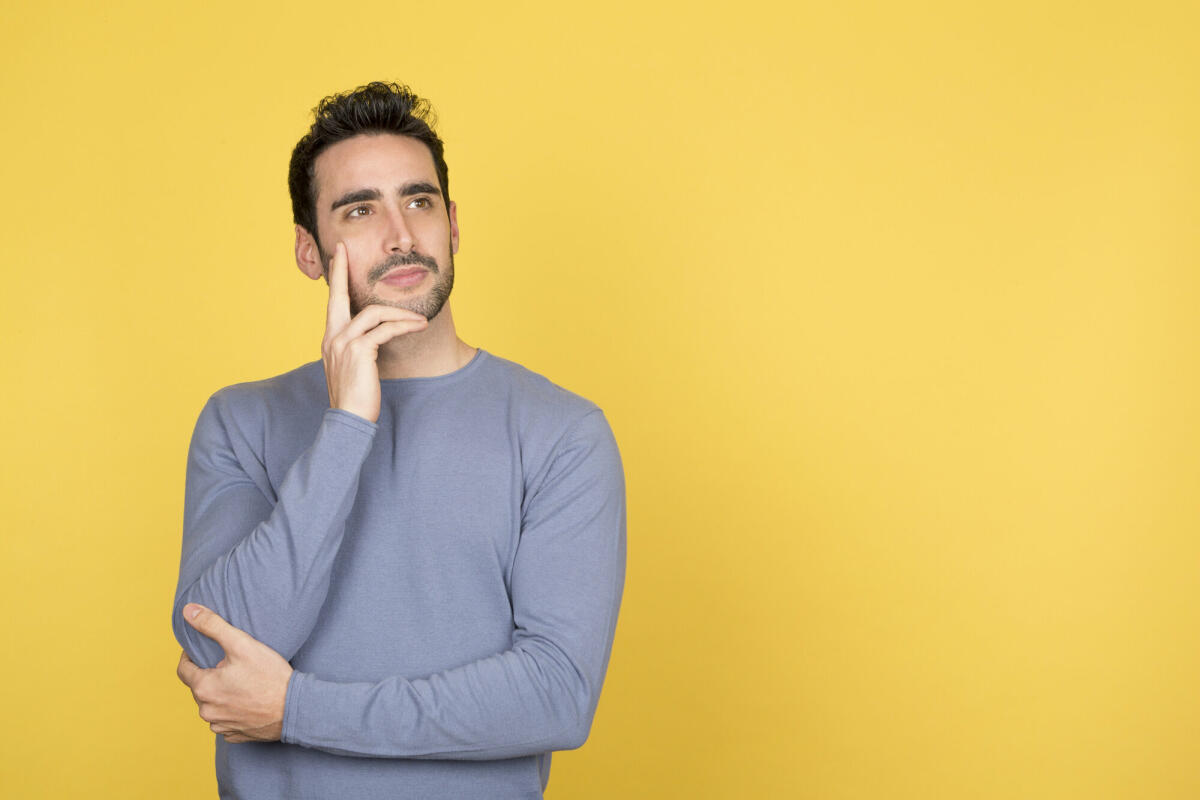 Nachdenklicher junger Mann mit einem ruhigen Gesichtsausdruck, der auf den Kopierraum blickt © Luisrojasstock / Getty Images