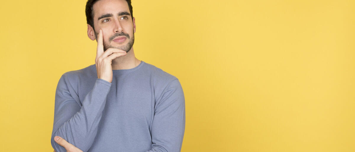 Nachdenklicher junger Mann mit einem ruhigen Gesichtsausdruck, der auf den Kopierraum blickt © Luisrojasstock / Getty Images