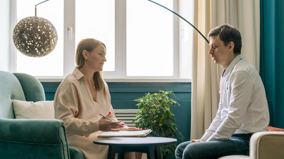 Eine Psychologin sitzt sich mit einem Klienten auf zwei Sesseln gegenüber. © Fiordaliso / Getty Images