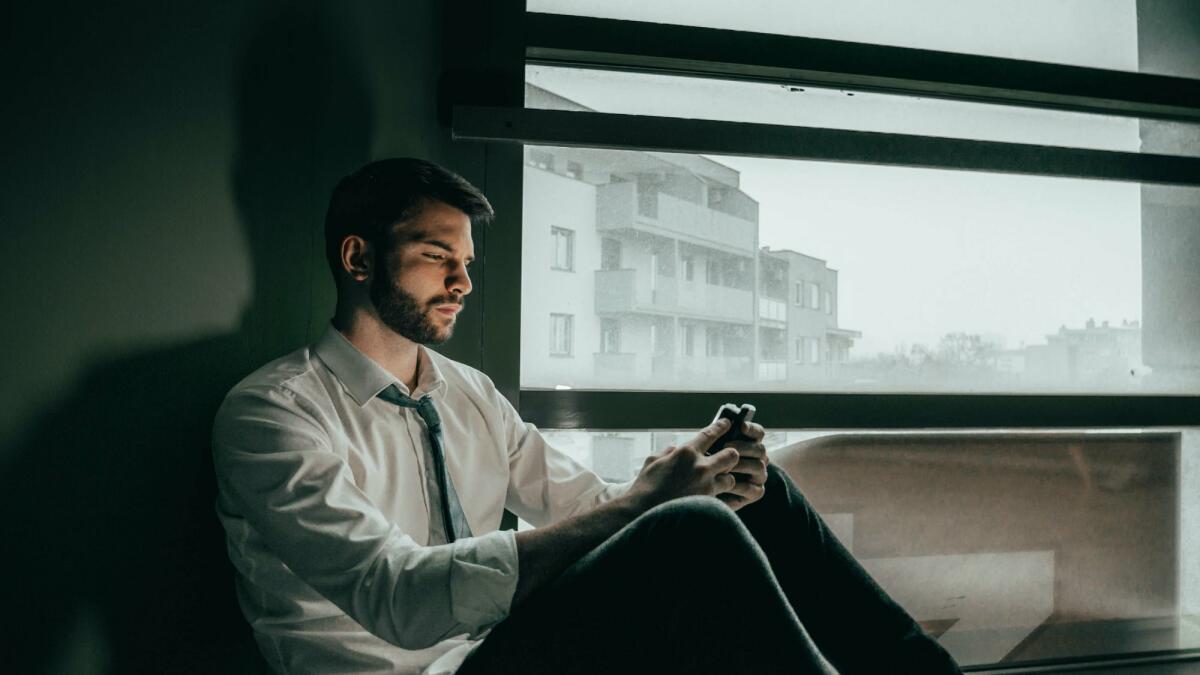 Ein Mann offensichtlich unglücklich sitzt auf dem Boden und hat sein Handy in der Hand  © Borna Hržina / Unsplash