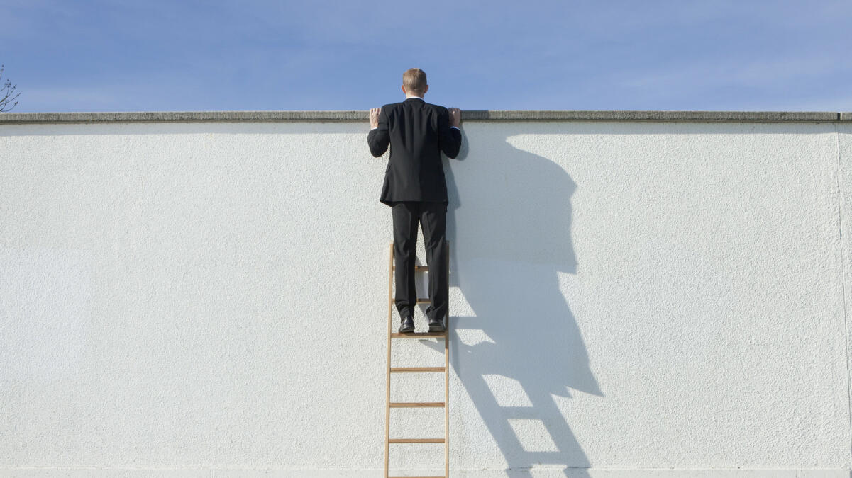 Geschäftsmann auf Leiter mit Blick über die Mauer  © Johnny Valley / Getty Images