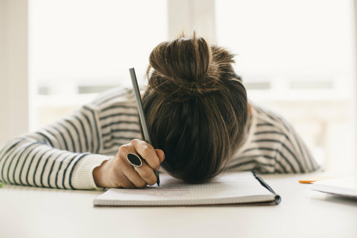 Frau liegt mit Kopf auf dem Schreibtisch.  © Westend61 / Getty Images