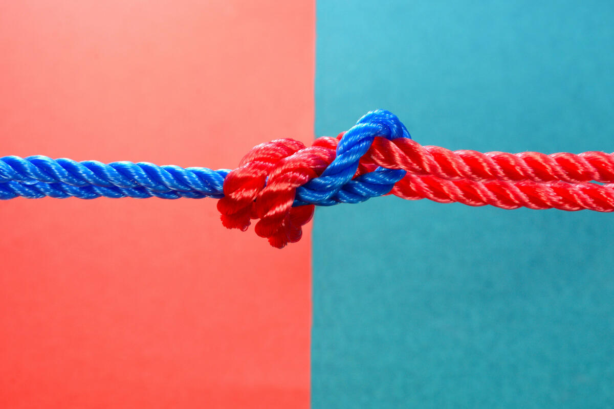 Roter und blauer Faden auf mehrfarbigem Hintergrund zusammengebunden © jayk7 / Getty Images