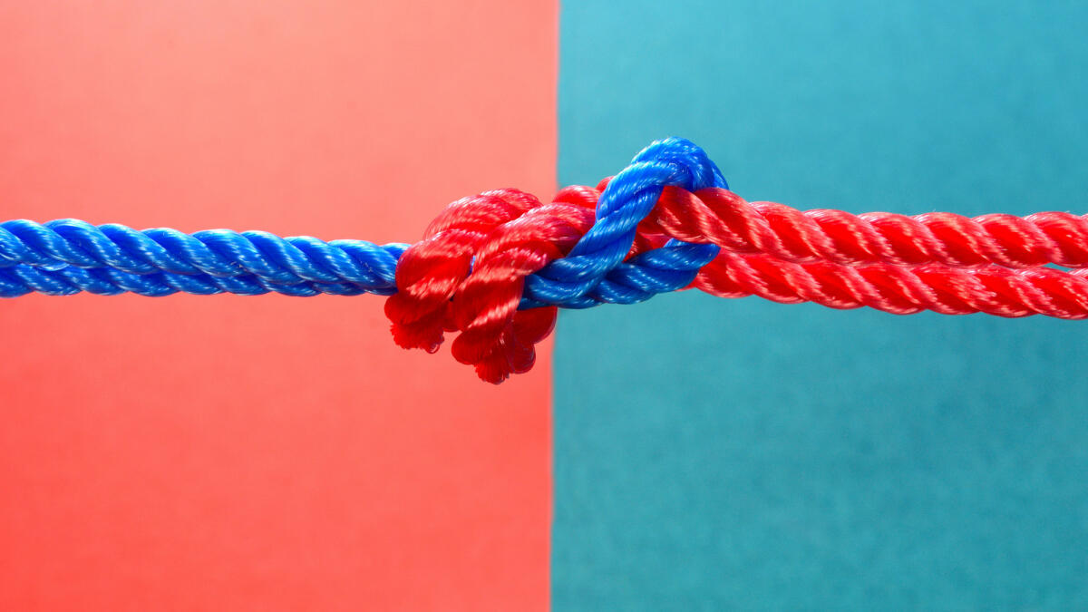 Roter und blauer Faden auf mehrfarbigem Hintergrund zusammengebunden © jayk7 / Getty Images