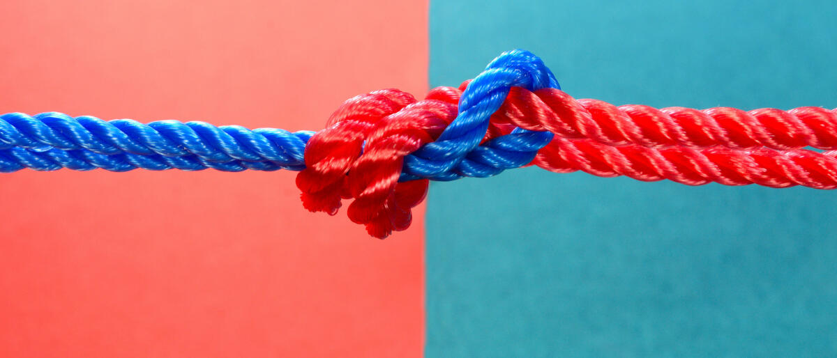 Roter und blauer Faden auf mehrfarbigem Hintergrund zusammengebunden © jayk7 / Getty Images