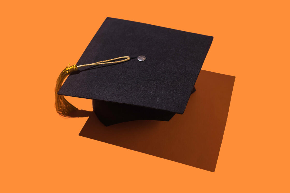 Schwarze Graduierungskappe mit goldener Quaste mit Schlagschatten auf orangem Hintergrund. © DBenitostock / Getty Images