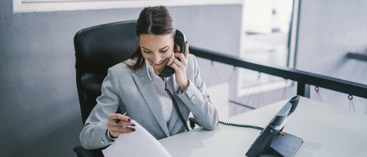 Eine Assistentin plant ein Geschäftstreffen am Telefon in einer Unternehmensfirma.