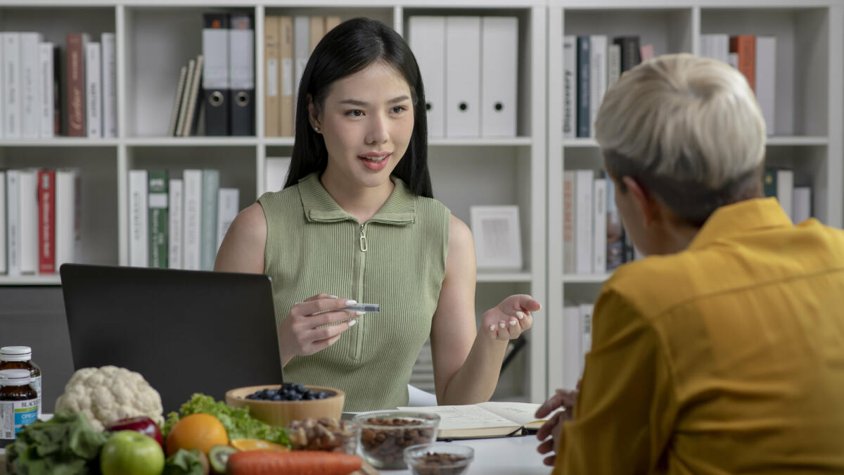 Ernährungsberaterin mit einer Kundin im Gespräch über einen Speiseplan und gesunde Produkte während einer medizinischen Beratung in der Praxis. © amenic181/ Getty Images