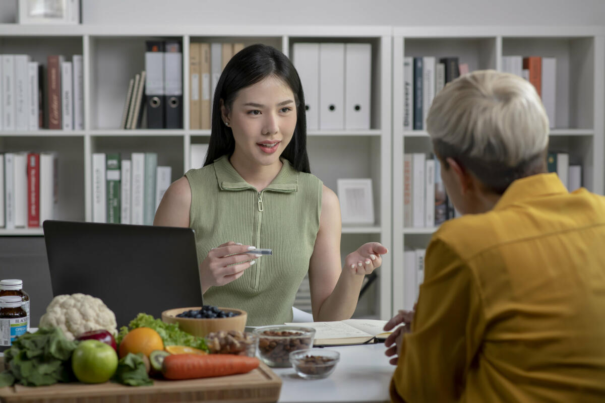 Ernährungsberaterin mit einer Kundin im Gespräch über einen Speiseplan und gesunde Produkte während einer medizinischen Beratung in der Praxis. © amenic181/ Getty Images