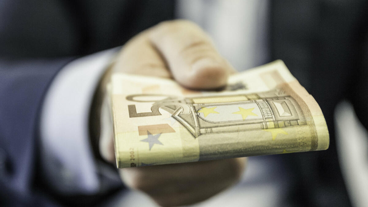 Nahaufnahme eines Geschäftsmannes, der gefaltete Fünfzig-Euro-Noten in der Hand hält © Manuel Sulzer / Getty Images