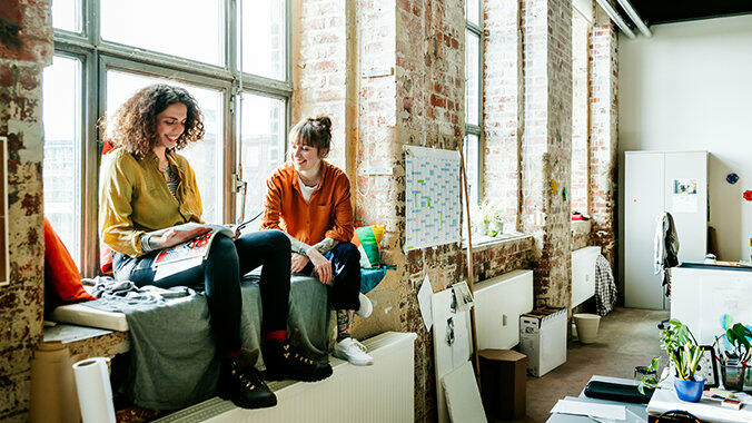 Zwei junge Frauen sitzen auf Fensterbank in Atelier © Hinterhaus Productions  / Getty Images