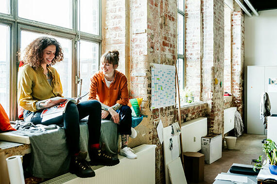 Zwei junge Frauen sitzen auf Fensterbank in Atelier © Hinterhaus Productions  / Getty Images