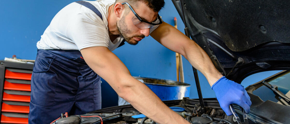 Ein Autowartungsmann überprüft den Automotor im Autoservice © ProfessionalStudioImages / Getty Images