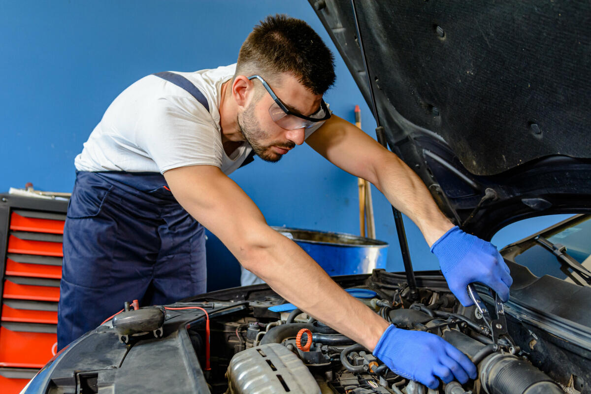 Ein Autowartungsmann überprüft den Automotor im Autoservice © ProfessionalStudioImages / Getty Images