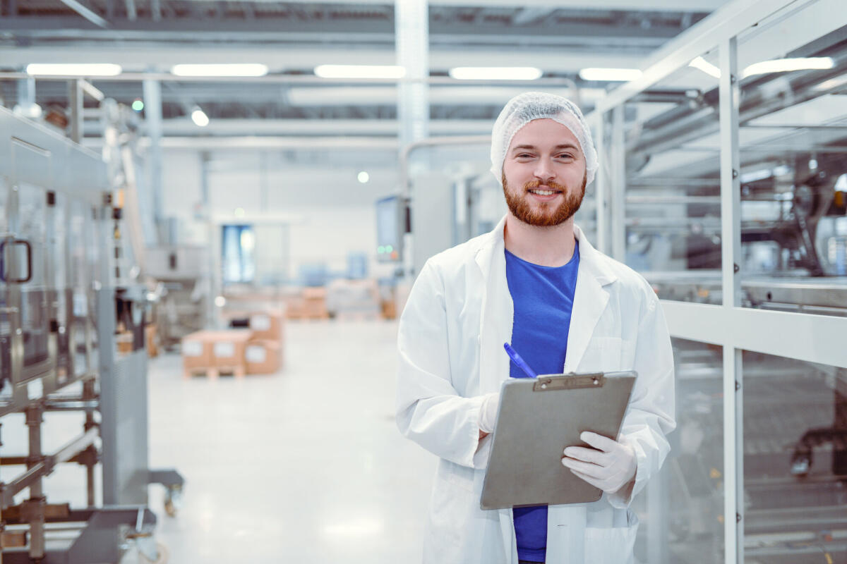 Gut aussehend lächelnd Nachwuchswissenschaftler mit Zwischenablage posiert in Fabrik  © Getty Images/ AleksandarGeorgiev