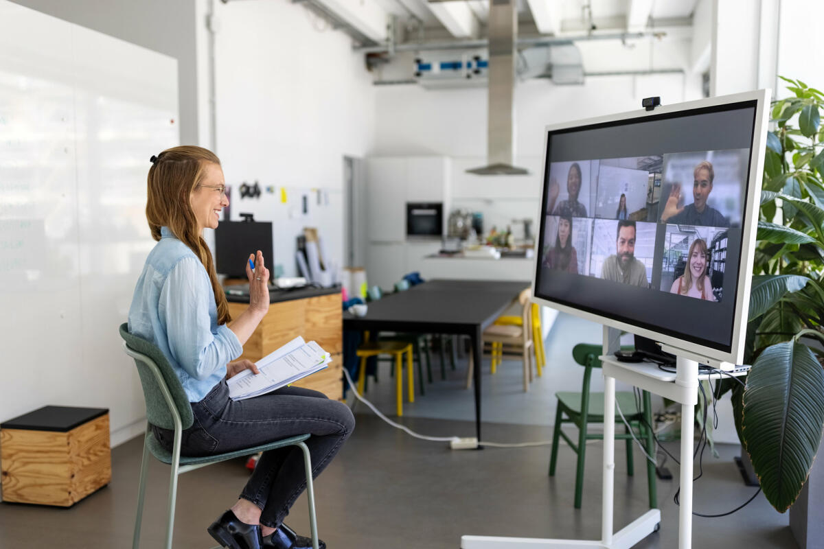 Frau im Videocall vor großem Bildschirm © Luis Alvarez / Getty Images