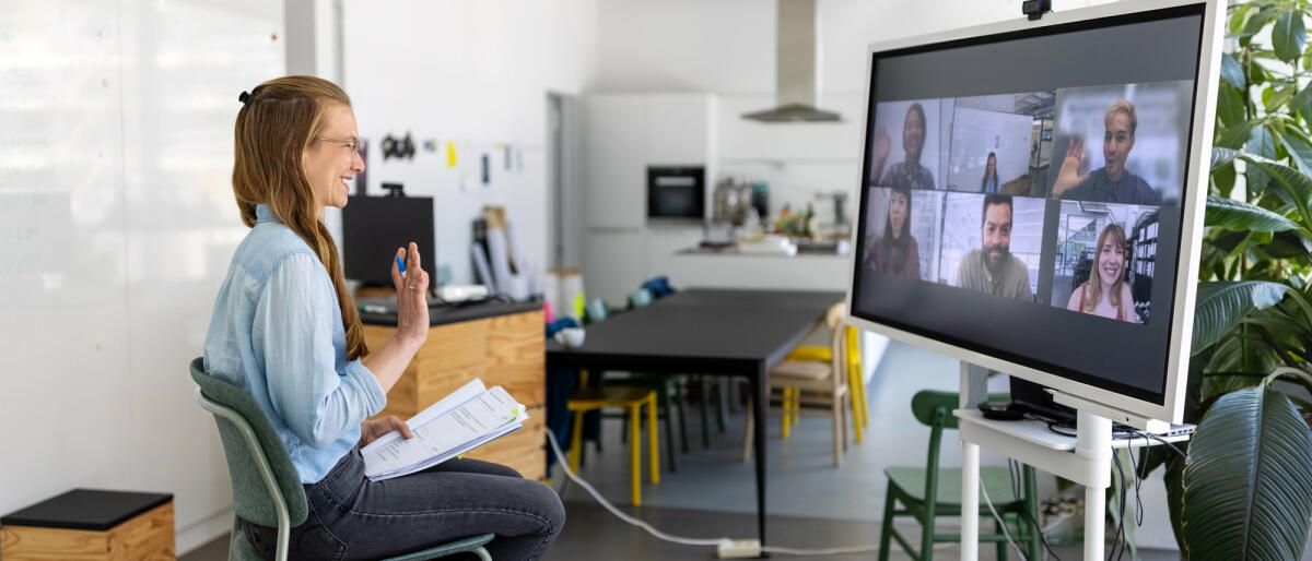 Frau im Videocall vor großem Bildschirm © Luis Alvarez / Getty Images