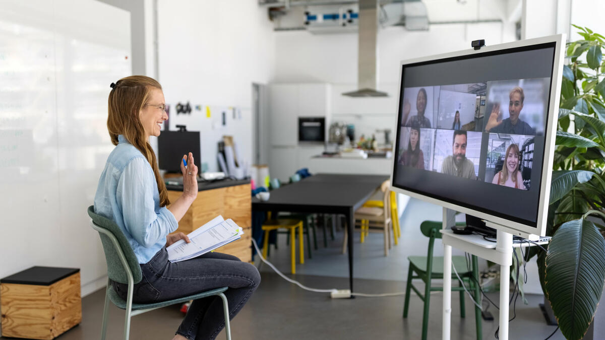 Frau im Videocall vor großem Bildschirm © Luis Alvarez / Getty Images