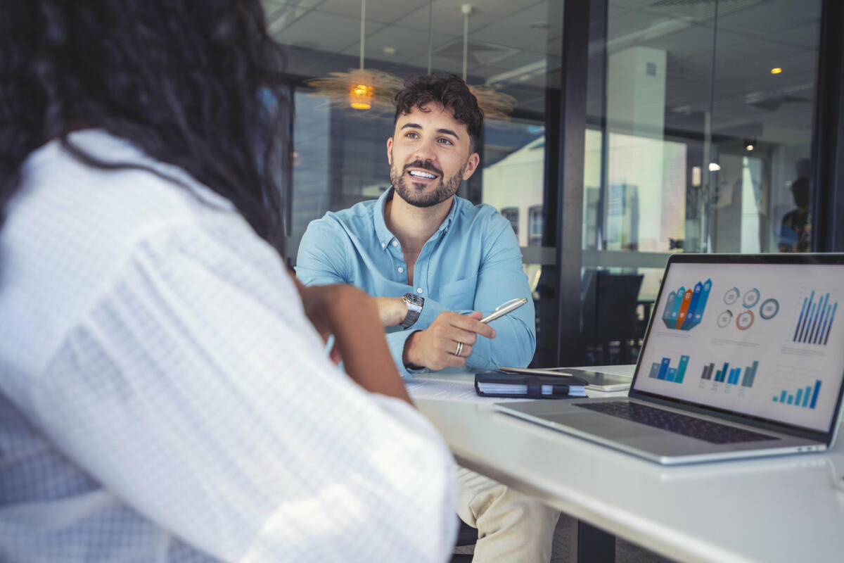 Junger Mann erklärt einer Kundin im Meeting etwas anhand von Charts auf dem Laptop © courtneyk / Getty Images