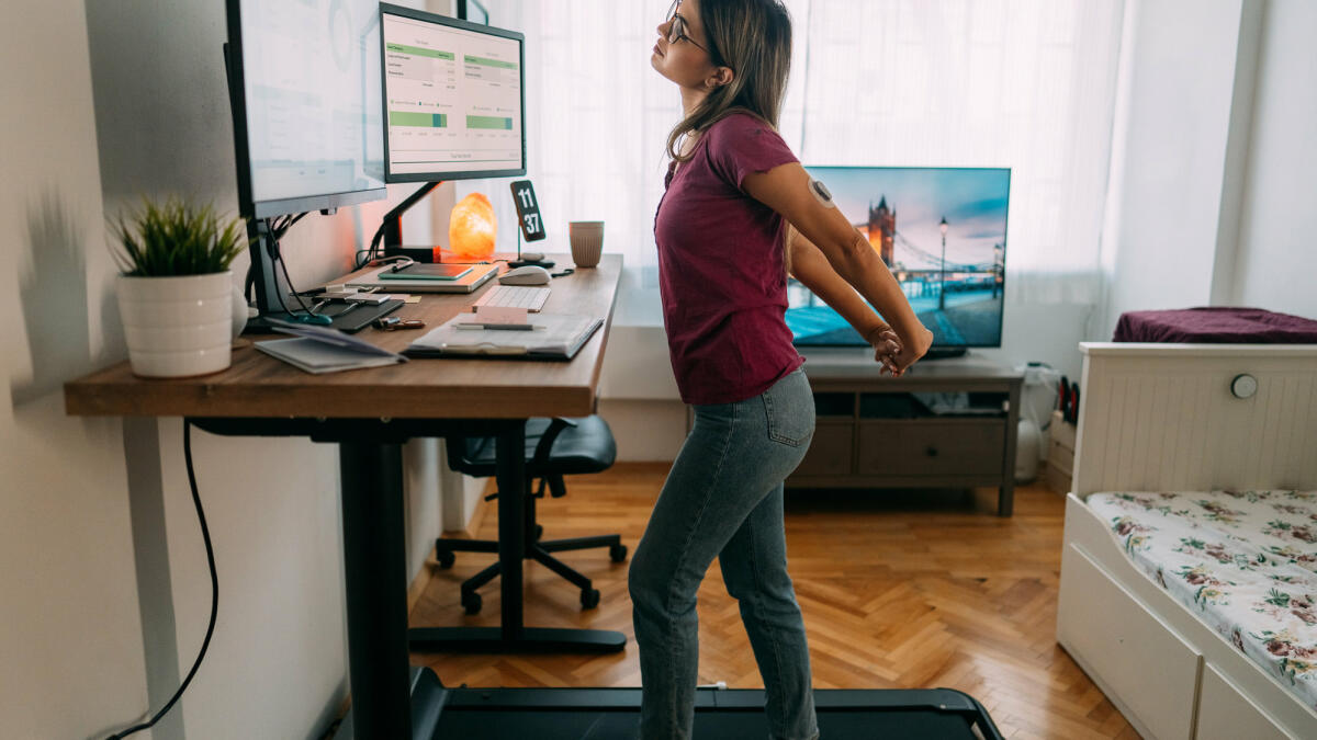 Frau im Homeoffice läuft auf dem Laufband unter dem Schreibtisch. © martin-dm / Getty Images