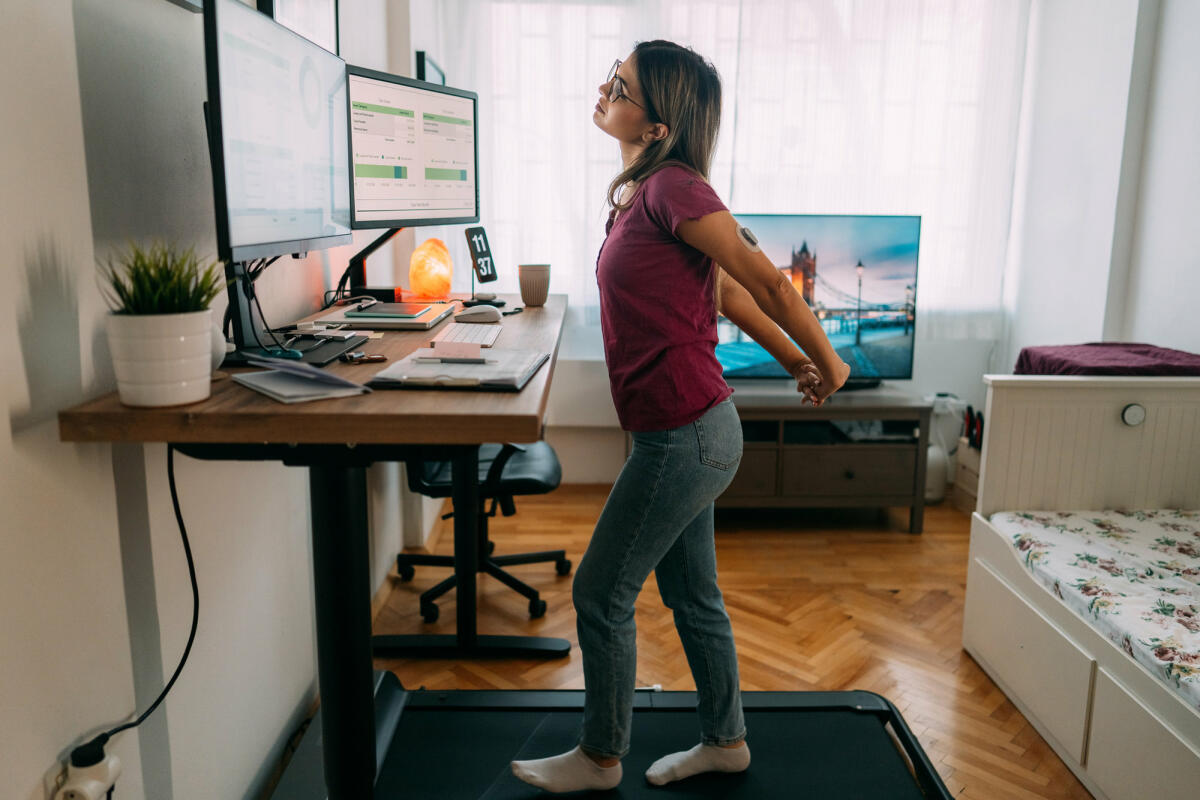 Frau im Homeoffice läuft auf dem Laufband unter dem Schreibtisch. © martin-dm / Getty Images