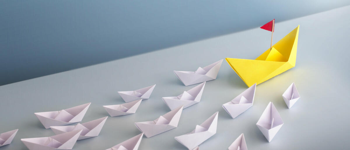 A group of origami white boat cruising to one direction lead by a bigger yellow boat. © Twomeows_IS / getty images