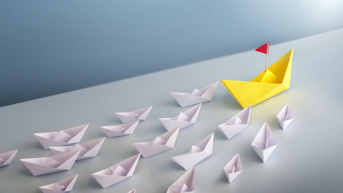 A group of origami white boat cruising to one direction lead by a bigger yellow boat. © Twomeows_IS / getty images