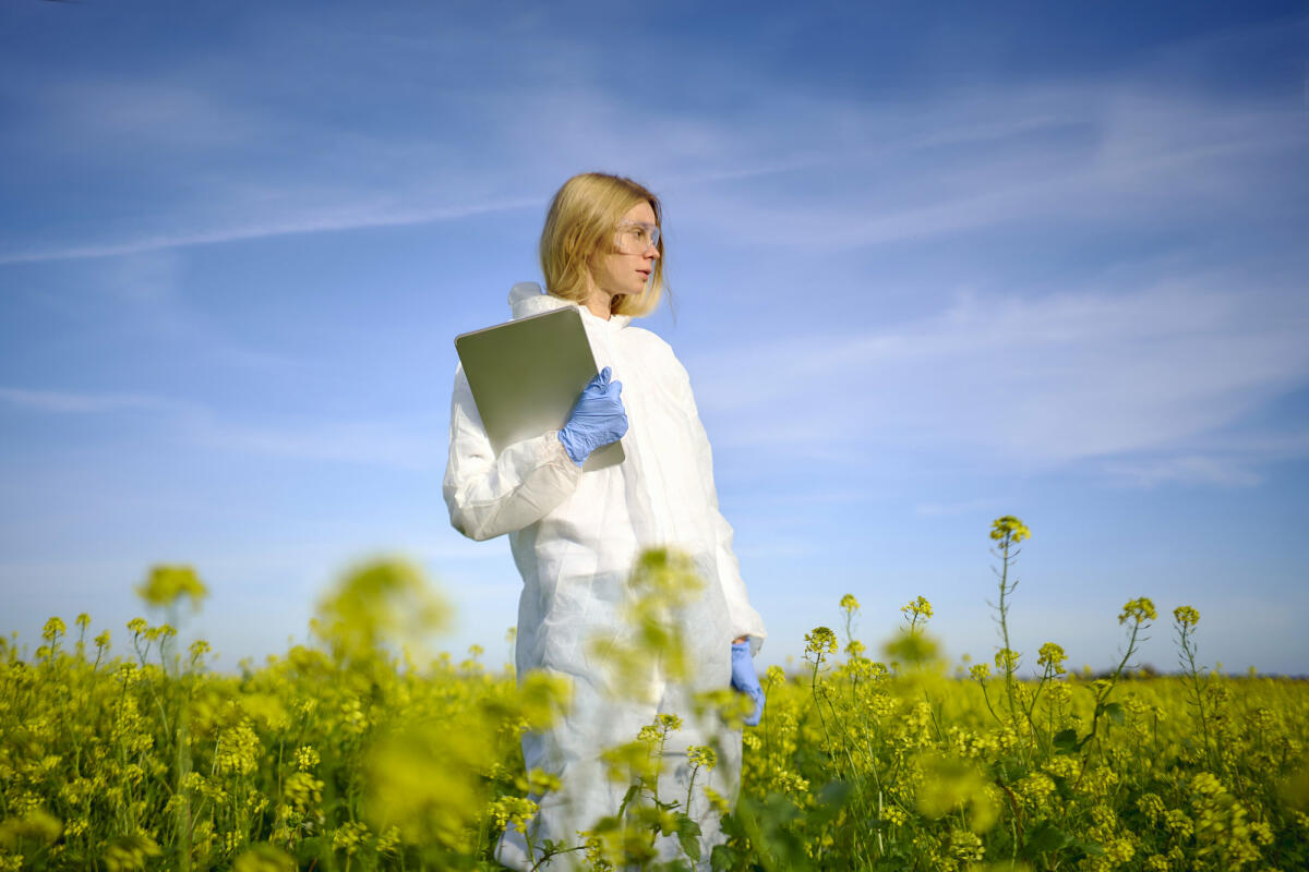 Eine junge Wissenschaftlerin steht im Schutzanzug mit einem Laptop in der Hand auf einem Feld. © Andriy Onufriyenko / Getty Images