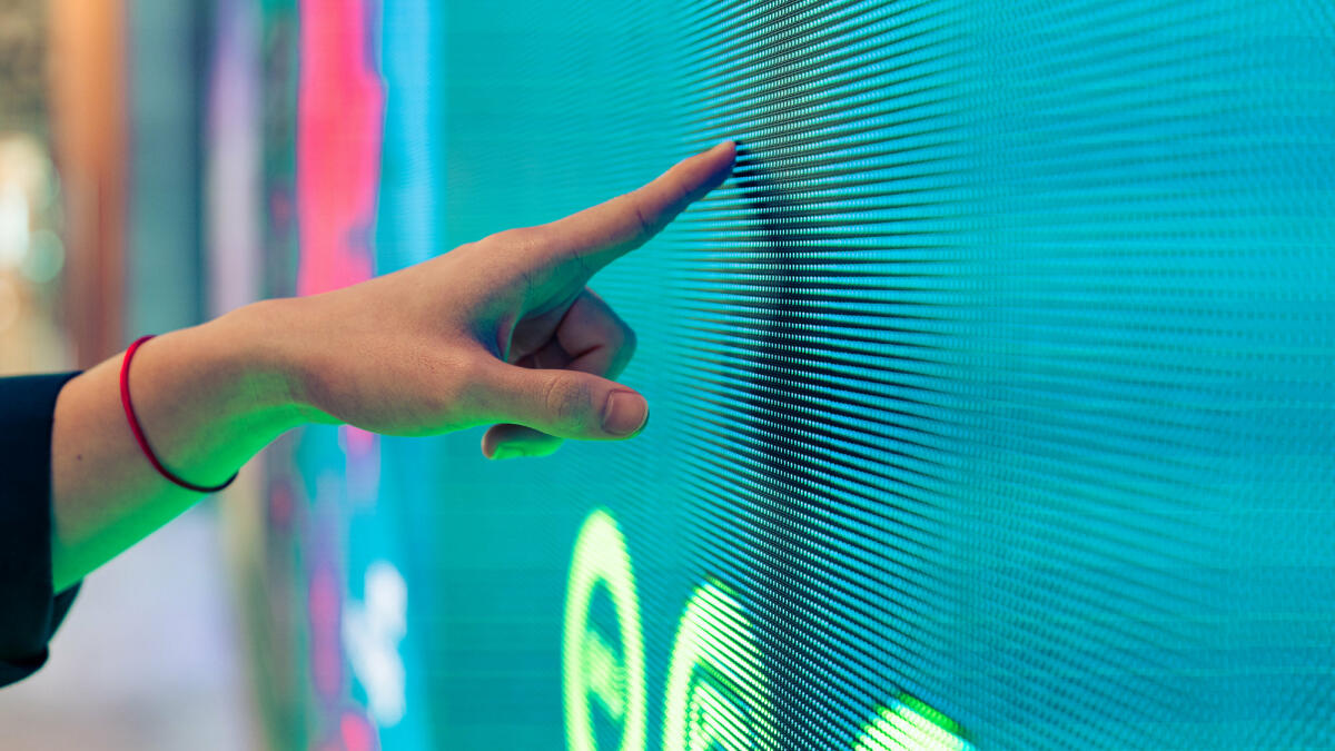 Nahaufnahme einer männlichen Hand, die eine beleuchtete Digitalanzeige im Dunkeln berührt © Jackyenjoyphotography / Getty Images