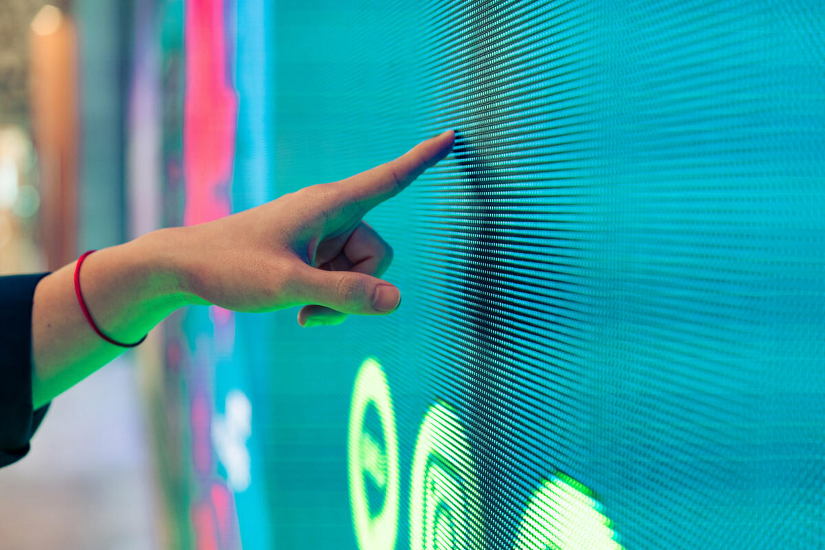 Nahaufnahme einer männlichen Hand, die eine beleuchtete Digitalanzeige im Dunkeln berührt © Jackyenjoyphotography / Getty Images