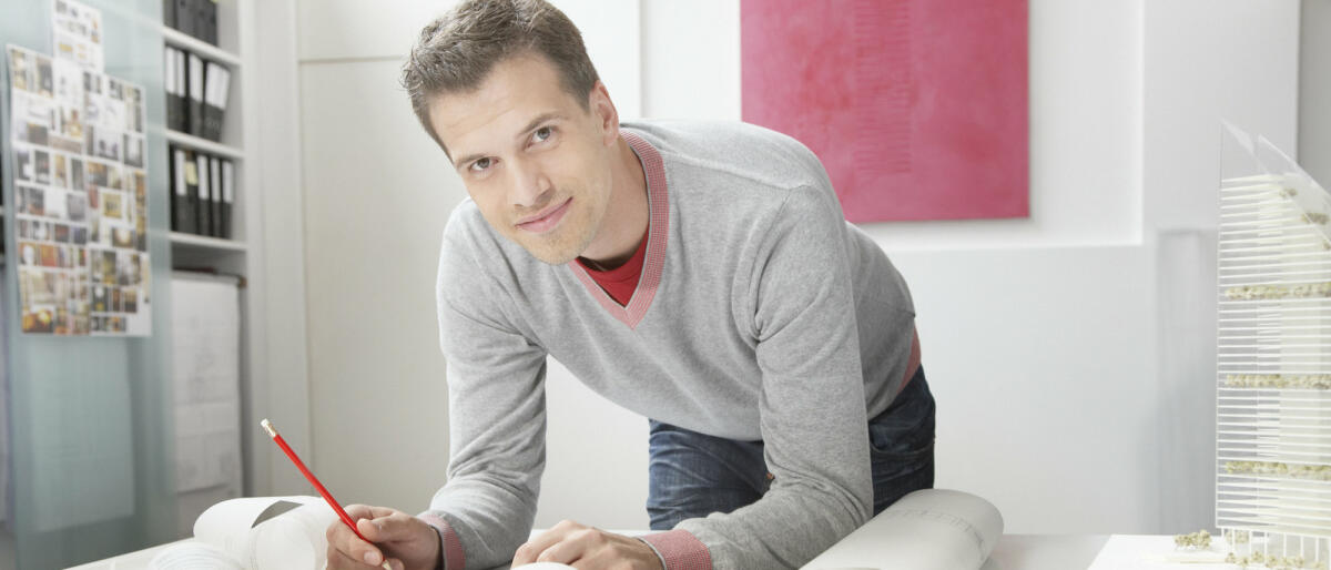 Junger Bauzeichner arbeitet an seinem Schreibtisch an einem Entwurf © Tom Merton / Getty Images