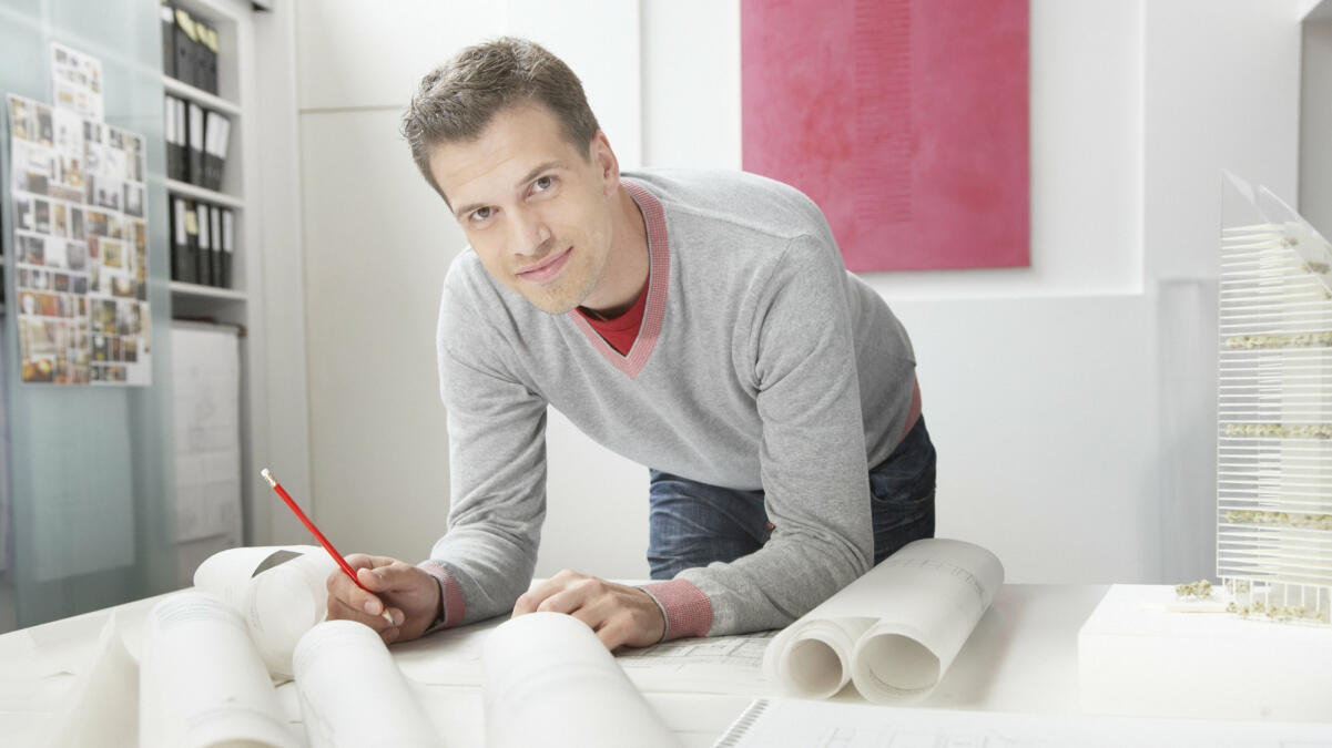 Junger Bauzeichner arbeitet an seinem Schreibtisch an einem Entwurf © Tom Merton / Getty Images