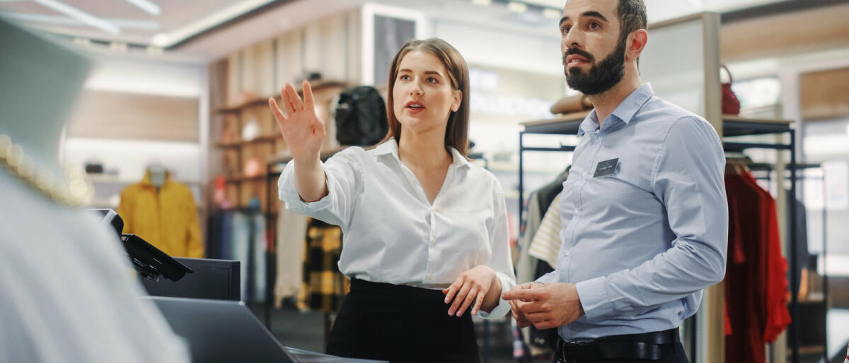 Bekleidungsgeschäft: Geschäftsfrau verwendet Laptop-Computer, spricht mit Visual Merchandising-Spezialisten und arbeiten zusammen. © Getty Images/ gorodenkoff