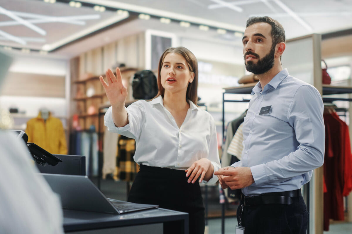 Bekleidungsgeschäft: Geschäftsfrau verwendet Laptop-Computer, spricht mit Visual Merchandising-Spezialisten und arbeiten zusammen. © Getty Images/ gorodenkoff