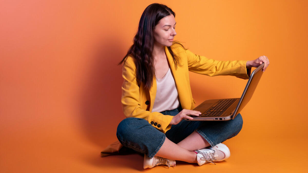 Junge Frau in Gelb macht Geschäfte an einem Laptop, ein Freiberufler oder ein Student arbeitet aus der Ferne. © Aleksandr Koltyrin / Getty Images