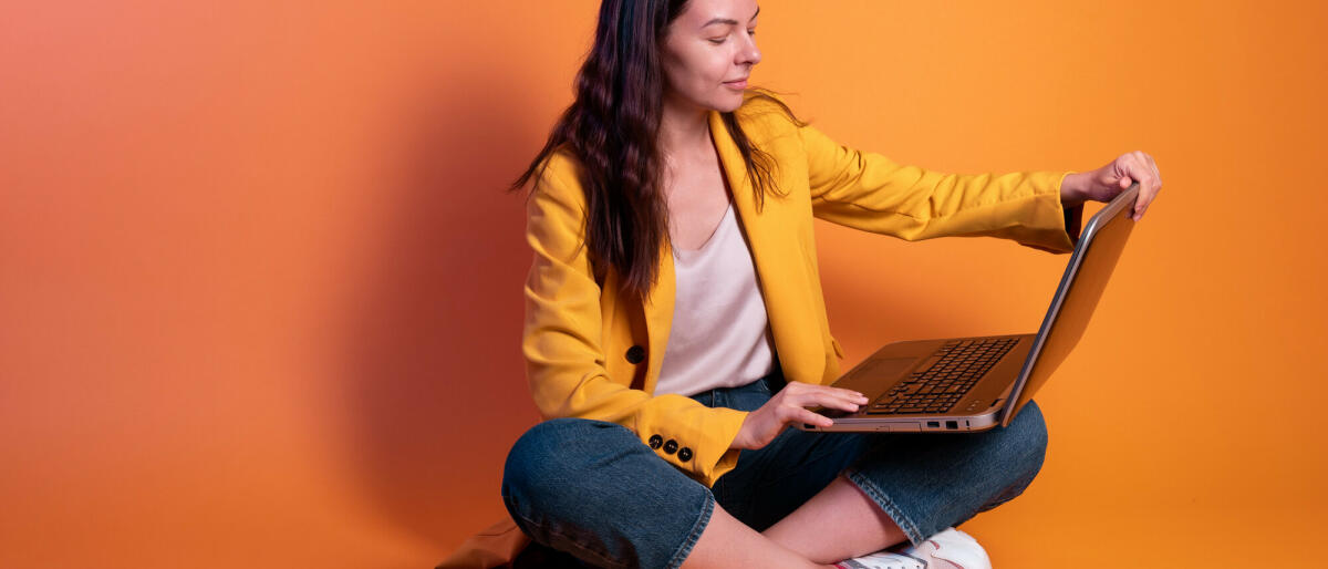 Junge Frau in Gelb macht Geschäfte an einem Laptop, ein Freiberufler oder ein Student arbeitet aus der Ferne. © Aleksandr Koltyrin / Getty Images