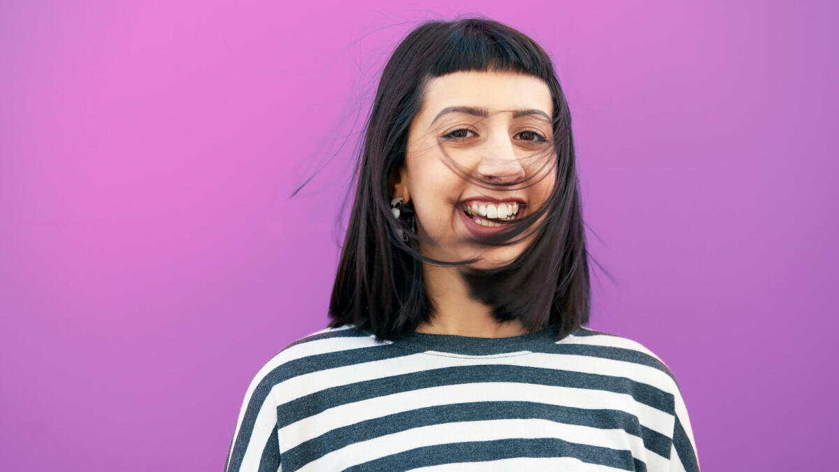 young woman in front of studio wall, laughing, hair swept into her face