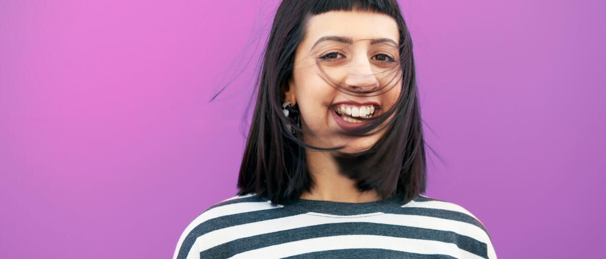 young woman in front of studio wall, laughing, hair swept into her face