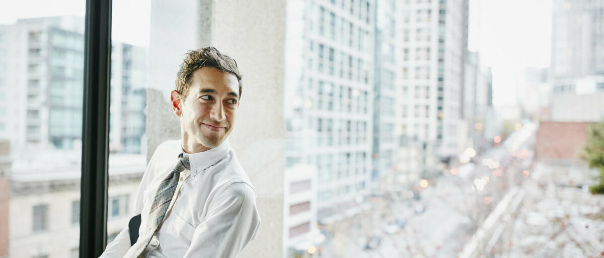 Geschäftsmann im Büro sitzend mit Blick auf die Stadt © Thomas Barwick / Getty Images