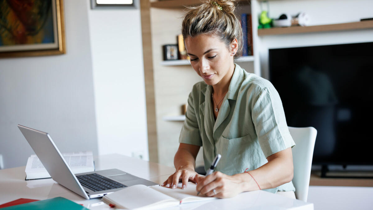 Schöne junge Frau, die sich Notizen macht, während sie von zu Hause aus lernt © bojanstory / Getty Images