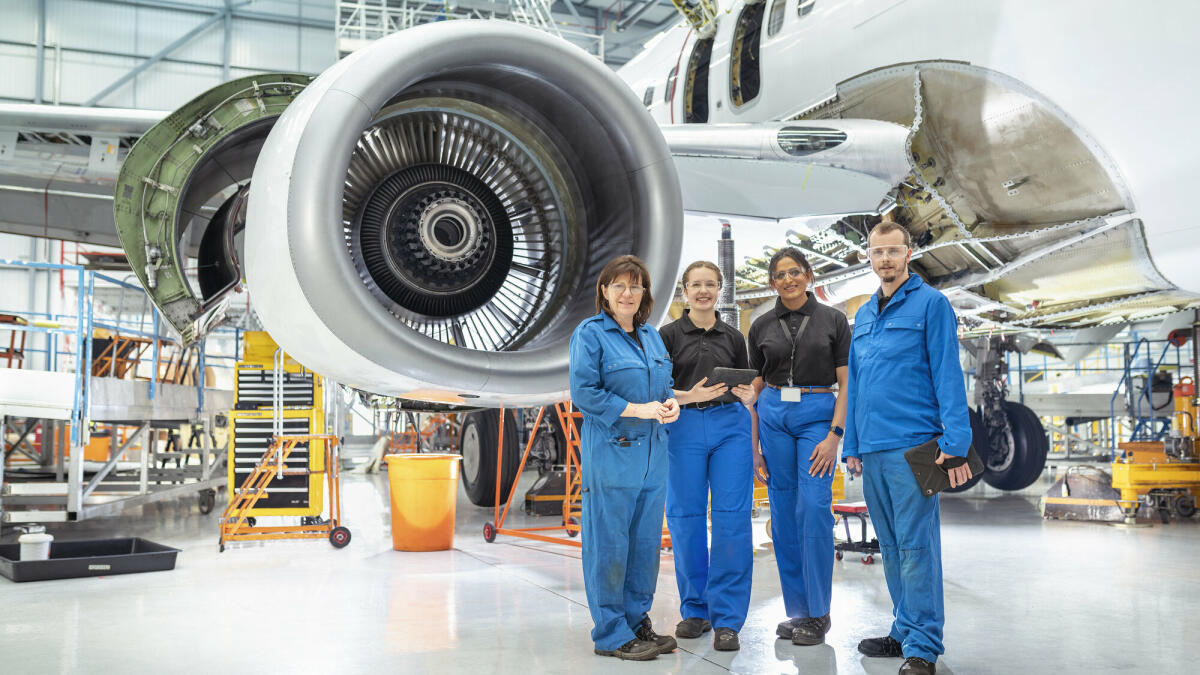 Eine Gruppe von Flugzeugingenieuren, in blauen Anzügen in einer Flugzeugwartungsfabrik. © Monty Rakusen/ Getty Images