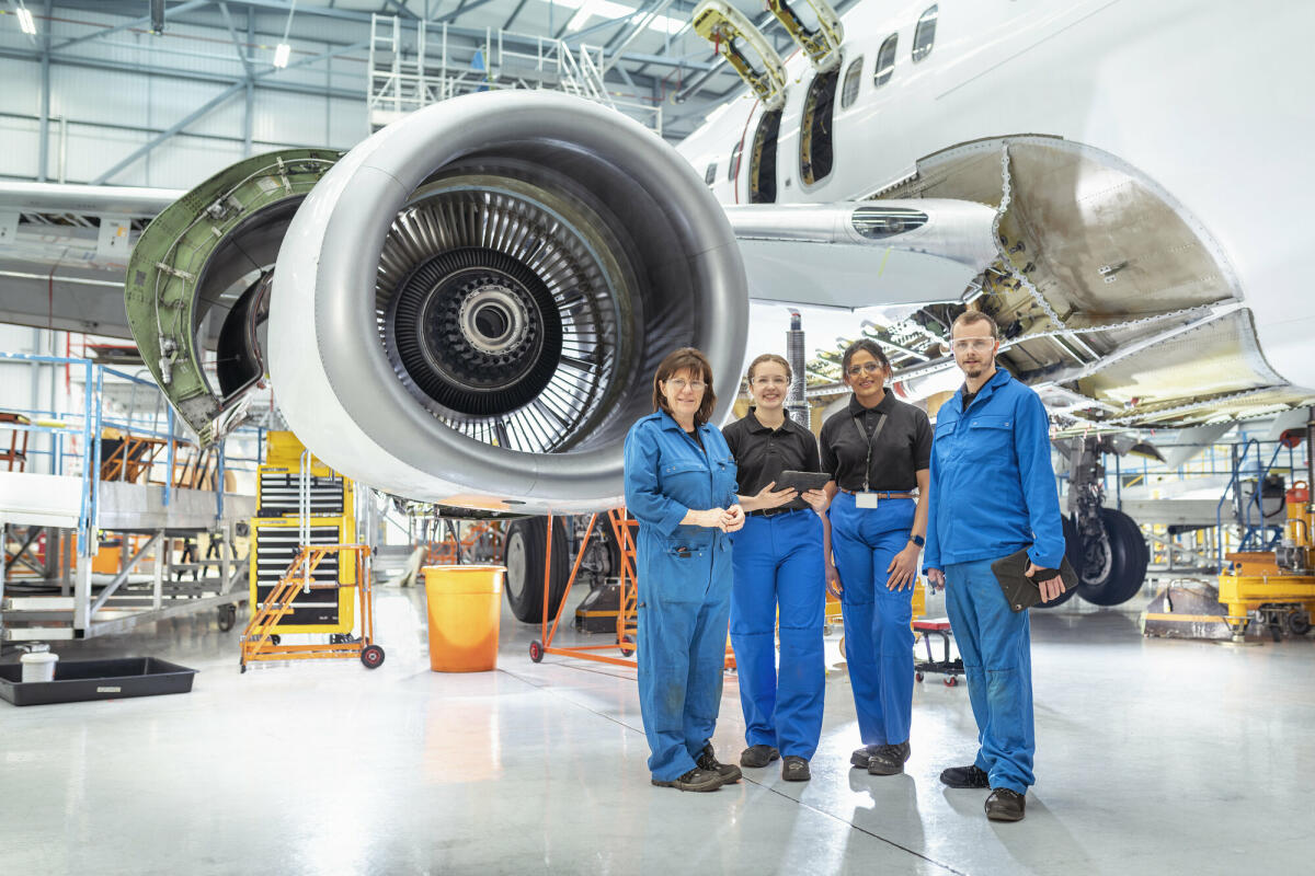 Eine Gruppe von Flugzeugingenieuren, in blauen Anzügen in einer Flugzeugwartungsfabrik. © Monty Rakusen/ Getty Images