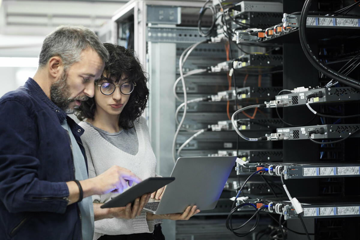 Männlicher Techniker zeigt einer Kollegin ein digitales Tablet. Ingenieur arbeitet mit einem Kollegen am Arbeitsplatz. Sie sind im Serverraum. © Getty Images/ 	Morsa Images