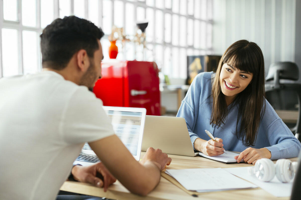 Mann und Frau im Büro lächeln sich an © Westend61 / Getty Images