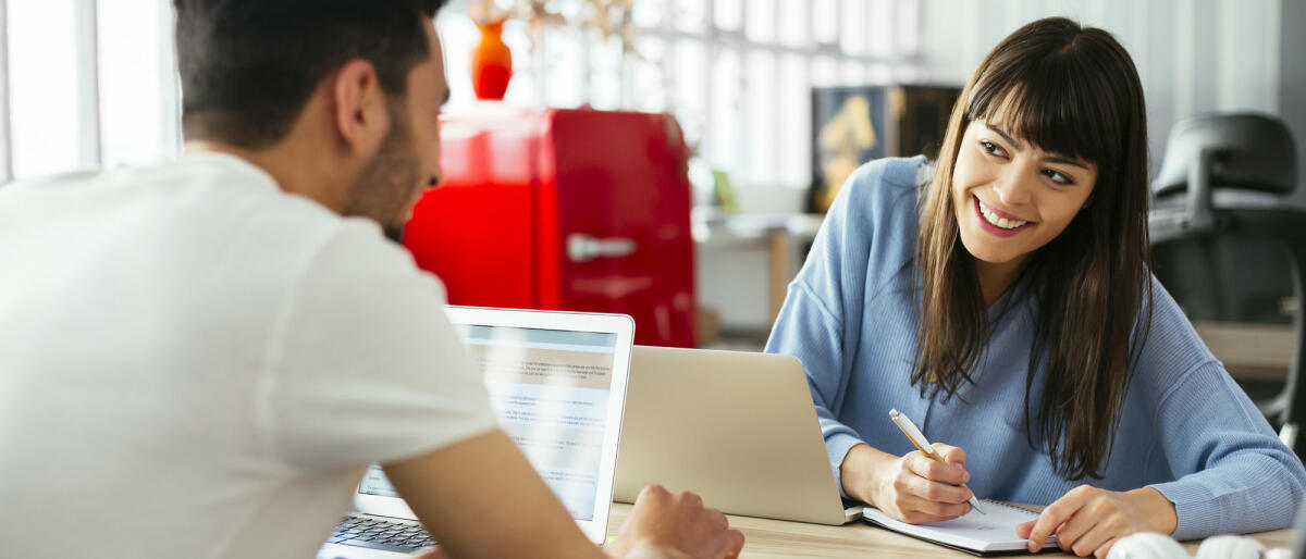 Mann und Frau im Büro lächeln sich an © Westend61 / Getty Images