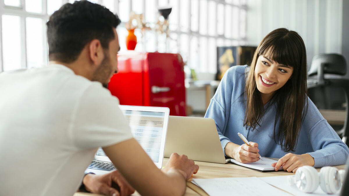 Mann und Frau im Büro lächeln sich an © Westend61 / Getty Images