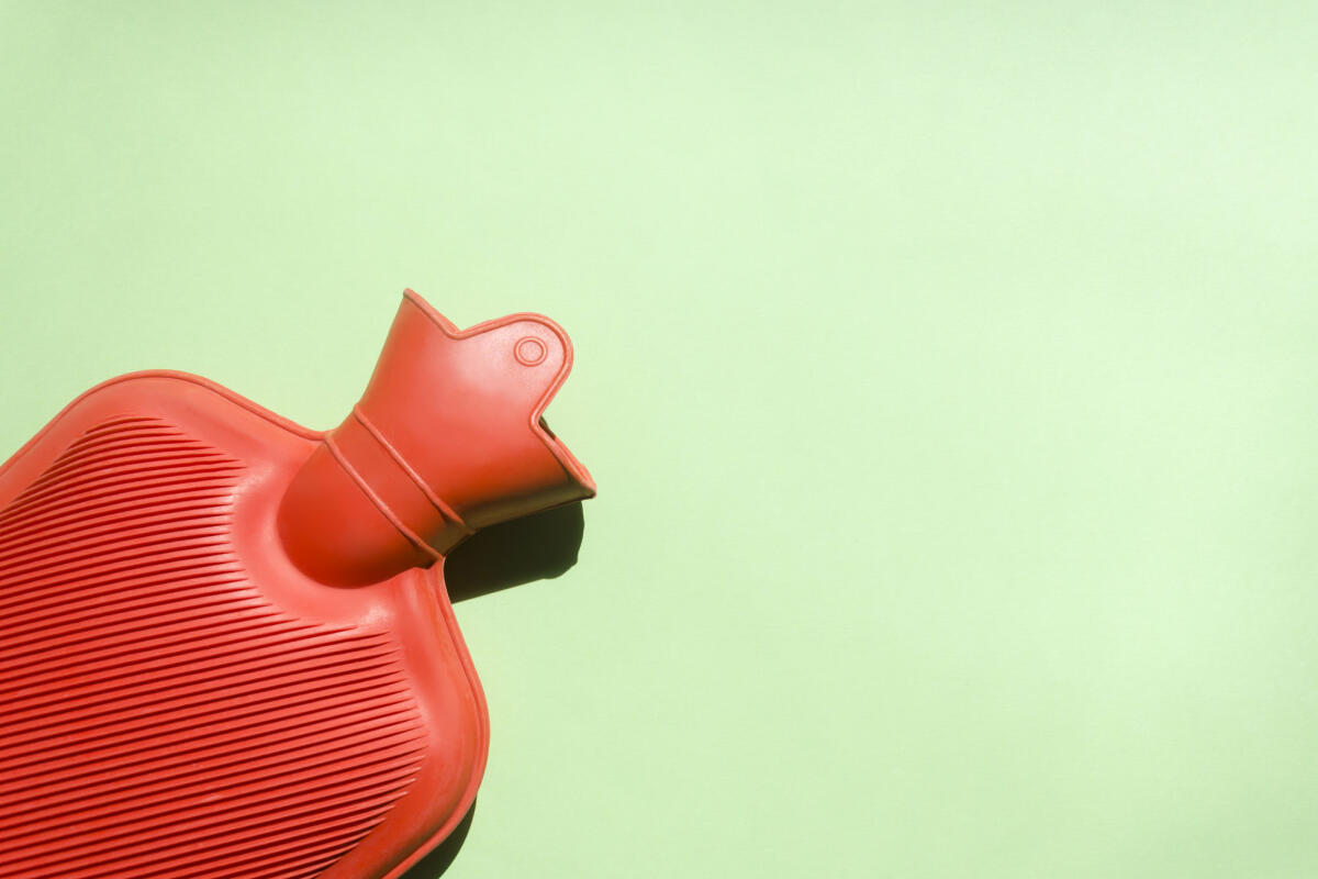 Rote Wärmflasche auf grünem Hintergrund. © Elizabeth Fernandez/ Getty Images